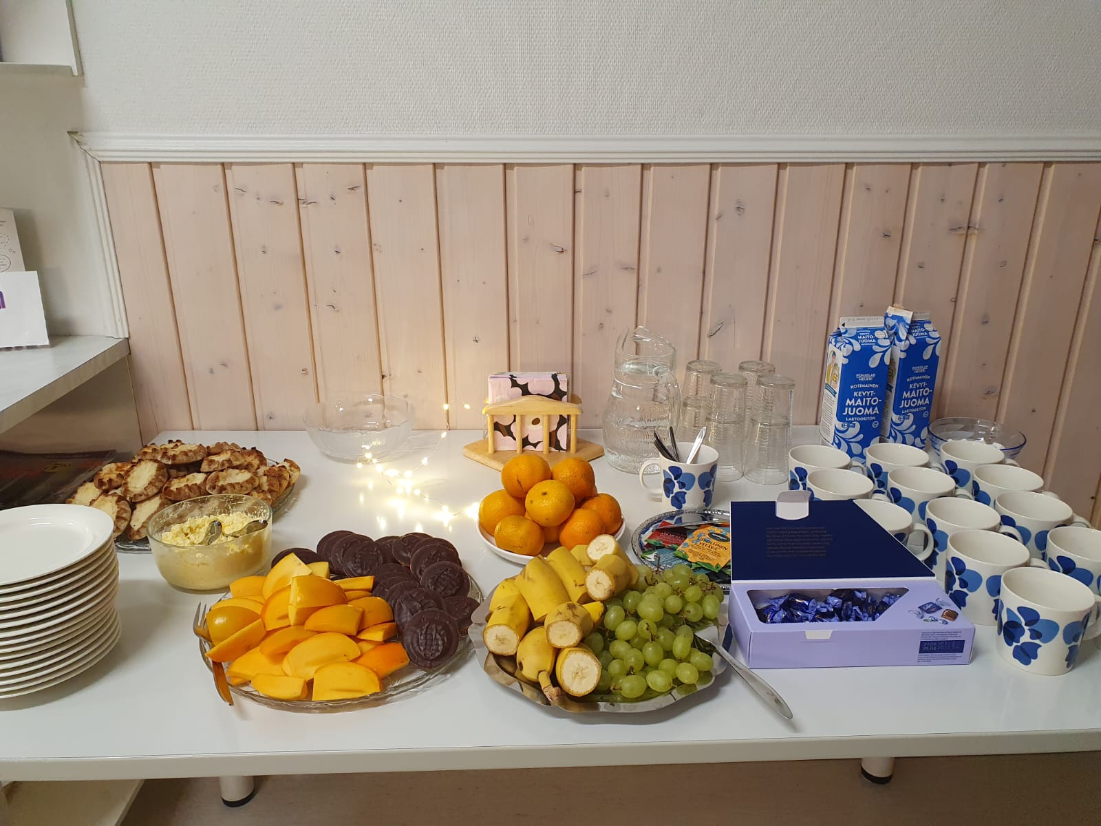 Valkoinen pöytä, jossa erilaista tarjottavaa, kuten suklaata, hedelmiä ja leipää.